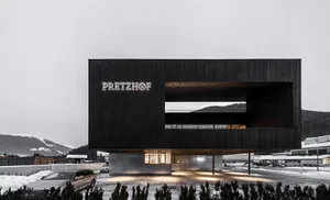 Black modern building with a glass front, natural light, and a car parked outside