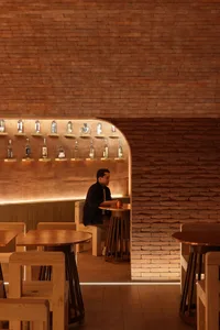A casual bar area with wooden tables and chairs, bottles, and a man sitting at a table