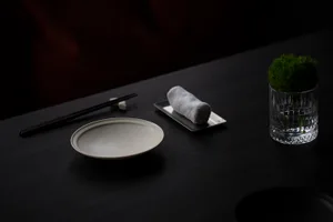 A dark room with a wooden dining table featuring two bowls, chopsticks, and a vase, creating an intimate ambiance