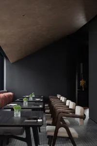 Modern restaurant interior with black walls, potted plants, and a dining area with tables and chairs