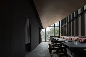 A modern restaurant interior with a large dining table surrounded by chairs, featuring a combination of black and white elements and dim lighting