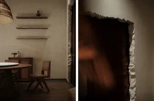 Dimly lit living area with a wooden dining table, chairs, vases, and a wall with decorative elements