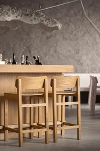 An empty bar area with wooden stools and tables, featuring a selection of bottles on the counter, creating a calm and inviting atmosphere