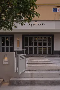 Modern restaurant facade with a concrete exterior, large windows, and potted plants, featuring two umbrellas for shade or decoration