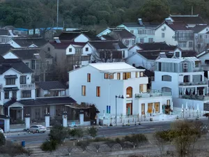 A modern house with a white exterior, multiple windows, and doors, situated in a residential area with trees and cars in the background