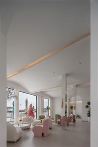 A modern living room with white walls, pink chairs, and three couches, featuring a dining table, decorative elements, and a warm atmosphere