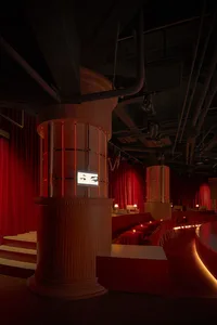 Elegant indoor event space with red curtains, seating areas, a dining table, and a TV screen, creating a sophisticated atmosphere