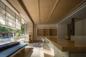 A well-lit restaurant interior with a large counter, wooden cabinets, and bookshelves, featuring a bench and natural light from windows