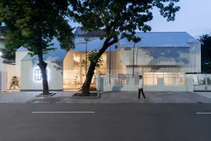 A modern building with a large window on its side, surrounded by chairs and a person walking by, conveying a calm and serene atmosphere