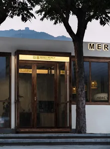 一座現代建築，擁有大型玻璃店面、白色外牆，入口處附近有一張椅子，周圍環繞盆栽植物