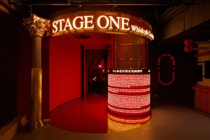 Modern interior design showroom with red walls, a red carpet, and a circular display reading Stage One, featuring two chairs and a dining table