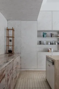 Empty kitchen with white walls and cabinets, featuring a minimalist countertop with several bottles, a cup, and a bowl