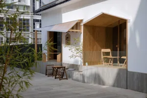 A modern patio with wooden chairs and tables, a potted plant, and a dining table in a clean and minimalistic design