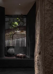 Indoor space with a black stone wall, a window, and potted plants on a table near the window, receiving sunlight