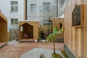 寧靜的戶外空間，設有兩座木造建築，一座花園棚屋與一座小型房屋／儲藏室，周圍環繞植物與樹木，並有休憩座椅