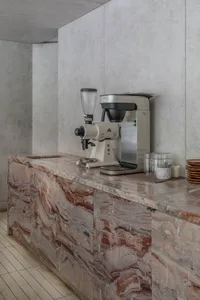 A modern kitchen with a marble countertop featuring two coffee makers and three cups arranged in different locations