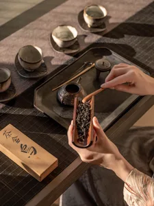 A person sits at a wooden table in an Asian setting, surrounded by cups, bowls, and a teapot, enjoying a meal and tea