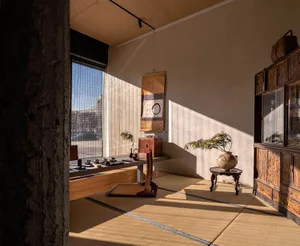 Warm and inviting living area with a wooden floor, two chairs, two dining tables, and decorative vases, illuminated by natural light through windows