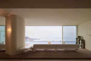 Open living space with large windows offering an ocean view, featuring a bench and two chairs for comfortable seating