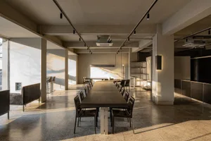 A well-lit conference room with a long black table surrounded by chairs, natural sunlight coming through windows, and a professional atmosphere