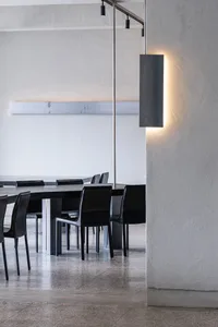 A modern restaurant with a long wooden dining table surrounded by multiple chairs, lit by a metal lamp and featuring a clean and contemporary design