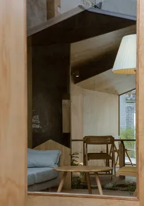 A living area with wooden floors and walls, featuring a couch, chairs, a potted plant, and a dining table, creating a cozy atmosphere for relaxation and socializing