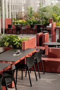 A modern dining area with several tables and chairs, potted plants, and black furniture, set in a well-lit space