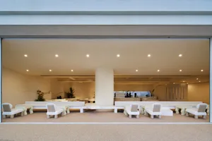 Open modern space with a large concrete wall, chairs, couches, and a potted plant, featuring clean lines and neutral tones