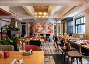 Inviting restaurant interior with wooden floors, tables, chairs, and potted plants, featuring wine glasses and a warm atmosphere