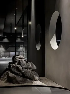 A modern living and dining space featuring a large rock in the center surrounded by other rocks, with two dining tables and a stylish atmosphere