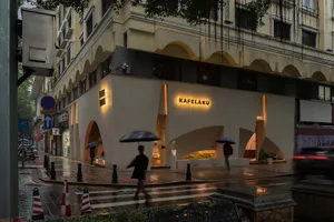 雨中的都市街景，現代店面與行人走在人行道上，有些人撐著雨傘