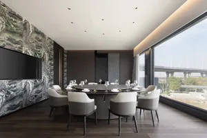 A modern dining area with a round table, chairs, and fine dining setup, set against a wood-floored background