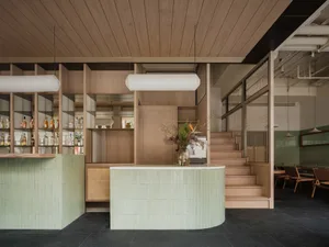 Industrial-style restaurant with wooden floors and walls, featuring two bars with green and white countertops, surrounded by bottles and vases