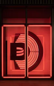 A neon sign in front of a window, reflecting the sign's vibrant colors and creating a lively urban atmosphere