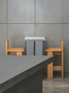 Minimalist dining space with two wooden chairs and a grey stone floor, featuring two dining tables and a focus on natural materials