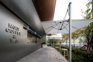 An inviting outdoor coffee shop with a modern design, featuring a large umbrella providing shade and comfort to patrons