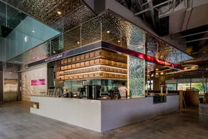 A cozy coffee shop interior with a bar area, chairs, cups, and bottles, creating a welcoming atmosphere for customers