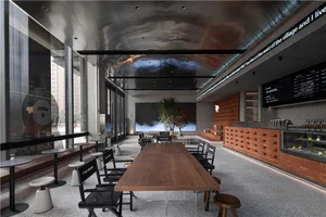 A well-lit restaurant interior with a large wooden dining table, potted plants, and natural light from windows