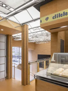 Modern kitchen with a glass display case, wooden elements, and natural light from a large window, set against a backdrop of a busy street