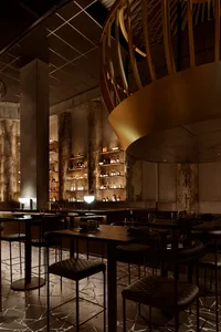 A cozy bar area with wooden tables and chairs, featuring bottles and wine glasses, set in a warm and inviting atmosphere