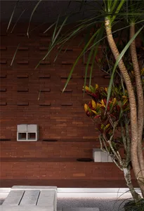 A serene outdoor courtyard with a brick wall featuring a window, two benches, and lush greenery