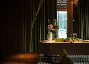 A well-lit dining space with a wooden theme, featuring a dining table, chairs, and potted plants, creating a warm and inviting atmosphere