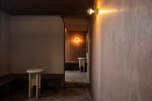 Dimly lit hallway with wooden walls and floors, featuring two small tables placed along the hallway