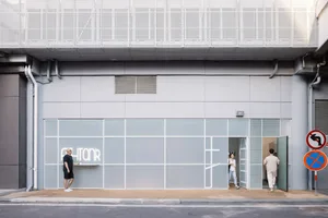 悠閒街景，人們注視著一棟大窗標有 PHIONR 的建築