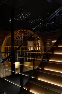 A staircase leads to a round dining area with multiple chairs and a table, surrounded by warm and inviting interior design elements
