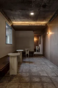 Empty dining area with a cement floor and white walls, featuring two small tables, a calm and quiet atmosphere