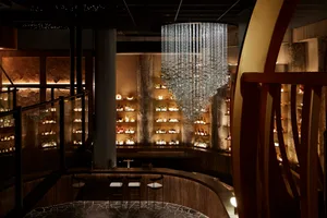 Elegant bar area with a chandelier, stools, and bottles on the counter, creating a sophisticated and inviting atmosphere