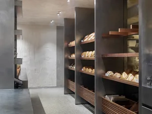 工業風麵包店，設有大型展示櫃陳列各式麵包，四周環繞裸露混凝土牆面與現代設計元素
