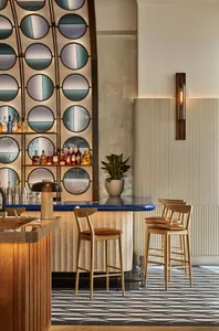 A casual bar area with a long wooden counter and multiple chairs, surrounded by bottles and perfect for socializing
