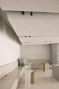 Empty living room with white walls and ceiling, featuring two couches, two chairs, a dining table, and decorative vases